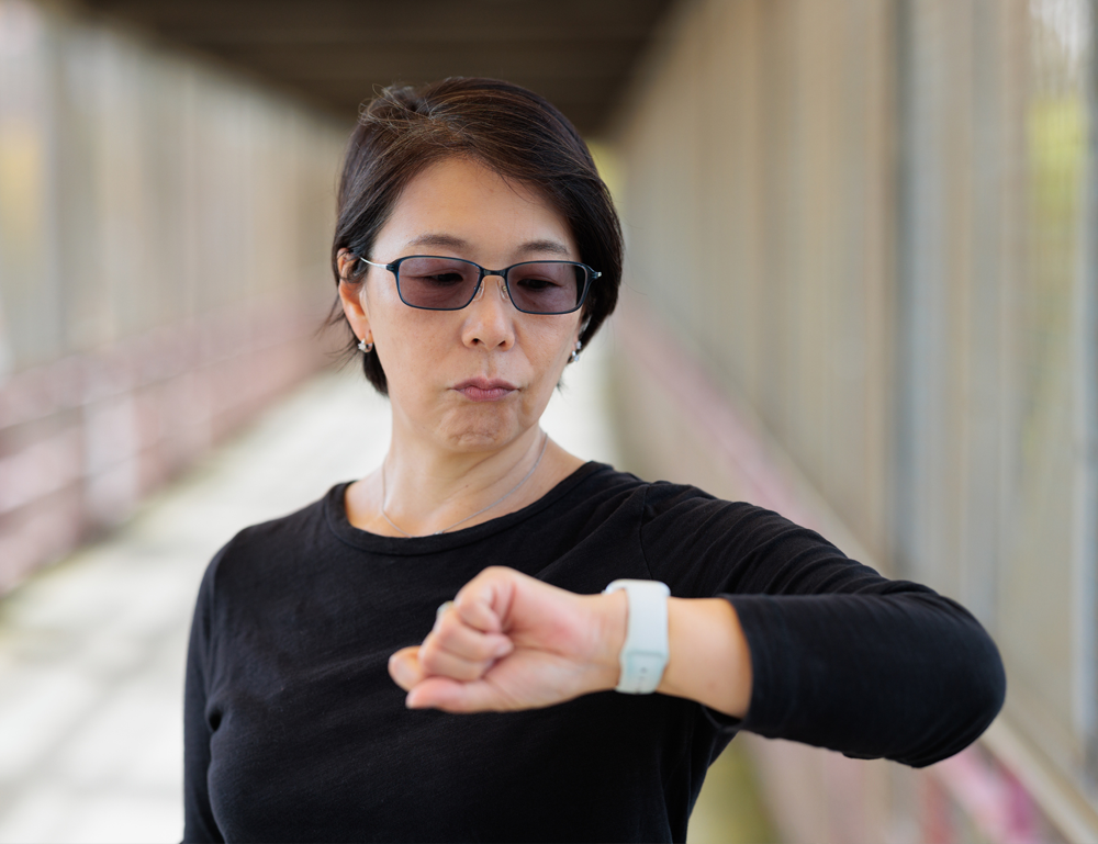 A woman with a serious expression looks impatiently at her wristwatch.