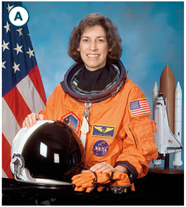 Ellen Ochoa is dressed in a NASA astronaut suit. Behind her is an American flag and, in the distance, a spacecraft.
